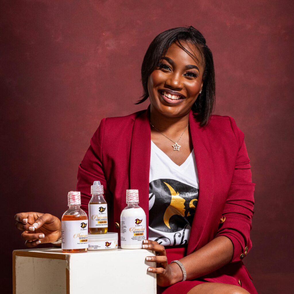 Businesswoman in burgundy blazer presenting skincare products while smiling in a studio setting.