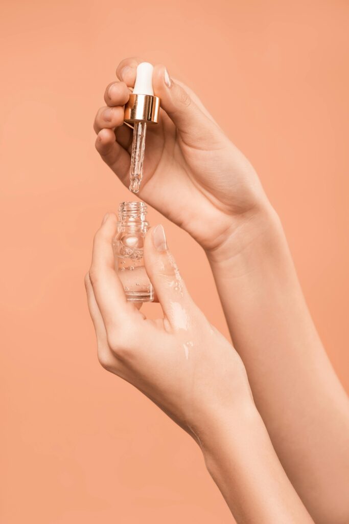 Close-up of hands using a dropper to apply skincare serum, ideal for health and beauty content.